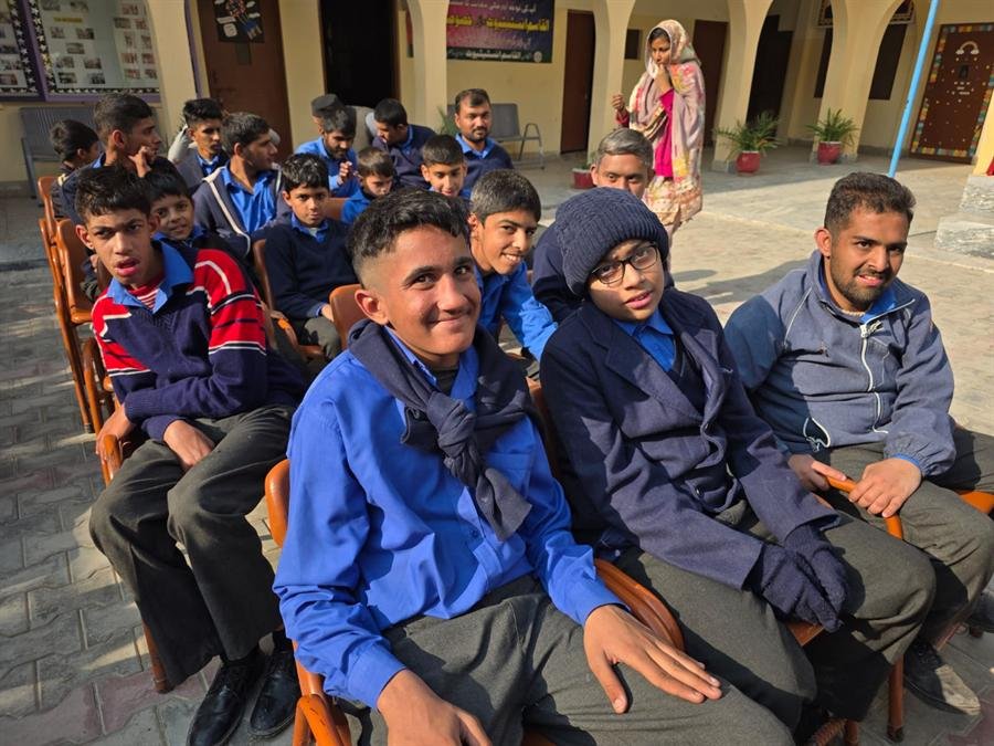 Rows of students and staff sitting on chairs in the courtyard, smiling at the camera