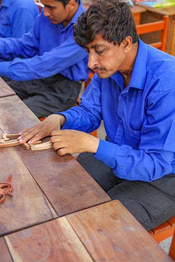 A student working on a small wooden craft at a wooden bench