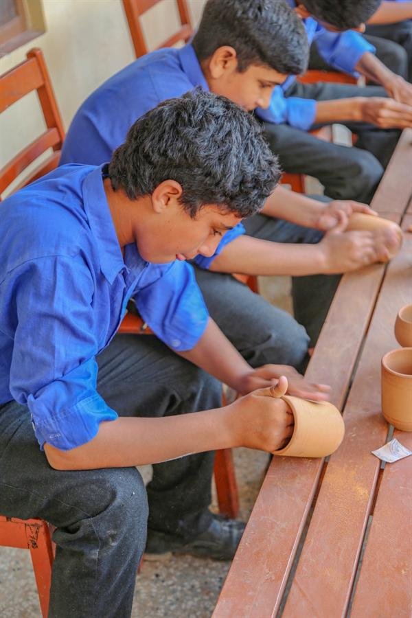 Students shaping small clay pots at a wooden bench