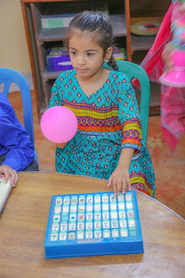 A young girl at a table with a pink balloon and a learning game board