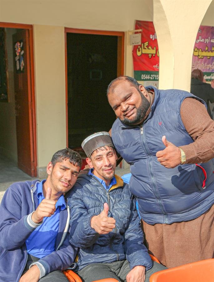 Two students and a man in a blue vest smiling with thumbs up in the courtyard