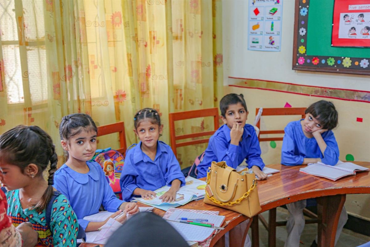 Young students in blue uniforms at their classroom desks, looking up at the camera
